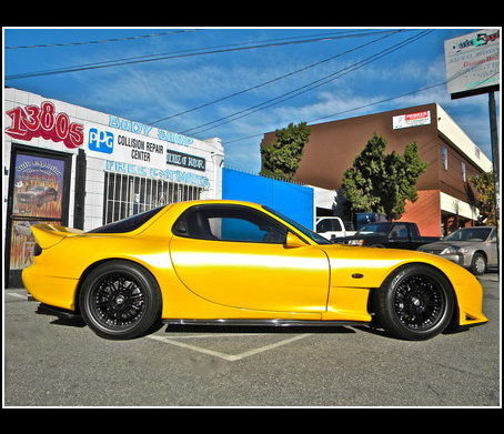 Yellow Mazda in front of the Auto Explosion shop sign